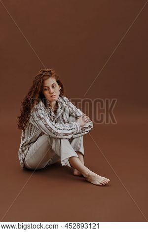 Portrait Of Young Red Haired Woman In Casual Clothing Sitting With Sad Sight Against The Brown Ginge