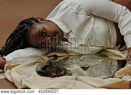 Portrait Of African Young Woman Lying Near The Mirror With Water Drops On Surface And Looking At Cam