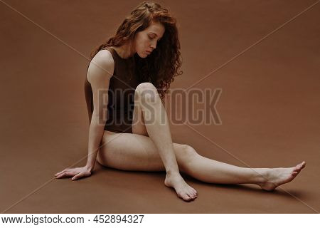 Portrait Of Young Woman With Red Curly Hair Sitting With Sad Expression Isolated On Brown Background