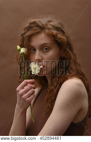 Portrait Of Young Pretty Woman With Curly Ginger Hair Holding White Flower Near Her Face And Looking