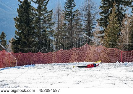 Tired Skier Lying On Snow Covered Landscape By Trees On Mountain