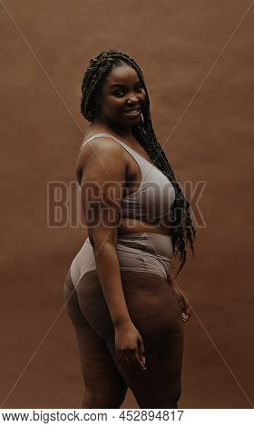 Portrait Of African Young Woman With Plump Figure Smiling At Camera Isolated On Brown Background