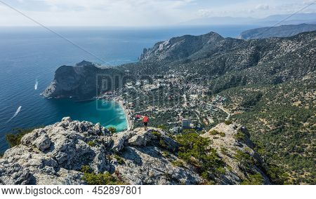 Man Traveller At The Top Of Falcon Sokol Mountain Enjoying Novyi Svit Town Below. Crimea