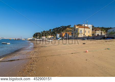 Trafaria, Portugal - March 1, 2022: Houses and bars along the seafront with wooden boats and pollutio at Trafaria, Portugal
