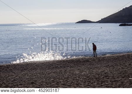 Scalea, Italy April 12, 2022: A Boy Stands On A Rocky Coast And Throws A Stone Into The Blue Sea In 