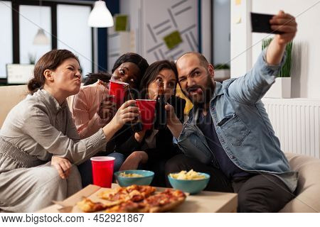 Diverse Group Of Colleagues Using Mobile Phone To Take Pictures At Office Party With Drinks After Ho