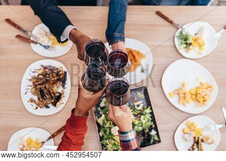 Zenith Shot Of 4 Hands Of Different Ethnicities Toasting With Red Wine