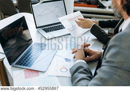 Office Desk With Gadgets And Documents. Successful Coworkers Sorting Documents, Learning Financial G