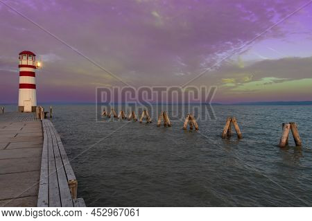 A Pier Leading To The Lake And A Red And White Lighthouse On Lake Neusiedl In Podersdorf, Austria. I