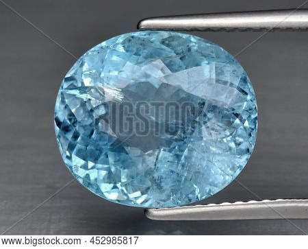 Natural Gemstone Blue Aquamarine In Tongs On A Gray Background