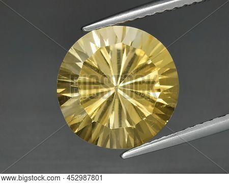Natural Gemstone Yellow Citrine In Tongs On A Gray Background