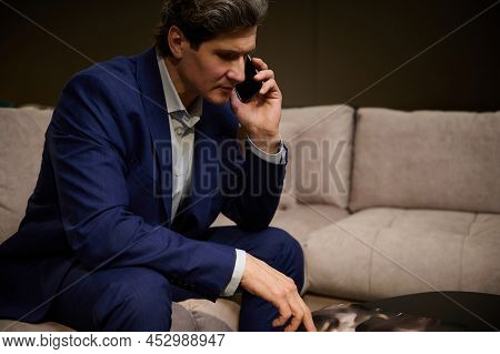 Handsome Mature Man In Business Suit Looking Furniture Catalogue And Talking On Mobile Phone, Sittin