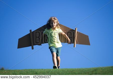 Child Boy Like A Pilot With Toy Wings Against Blue Sky. Kids Freedom Concept. Dreams Of Becoming A P