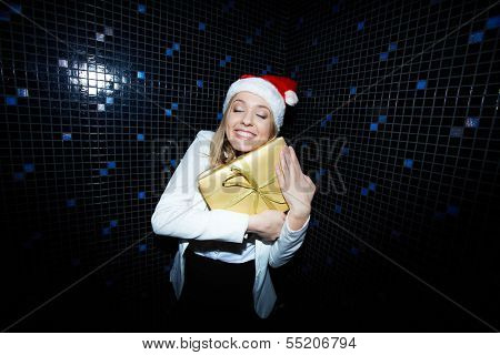Portrait of pleased businesswoman in Santa cap holding Chistmas gift