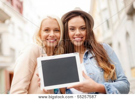 holidays, advertisement, technology and tourism concept - two beautiful girls toursits with blank screen tablet pc in the city