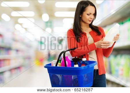 Beautiful brunette woman with basket reading label on cleanser in a shop