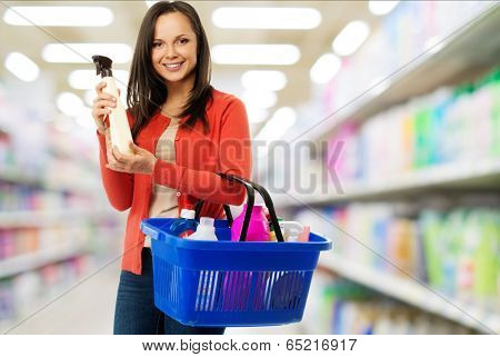 Beautiful cheerful brunette woman with basket full and bottle of cleanser in a shop