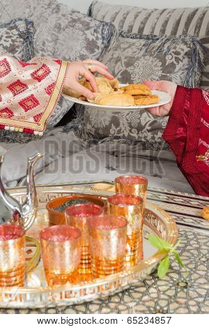 Hands of a moroccan woman presenting ramadan cookies and tea to a guest