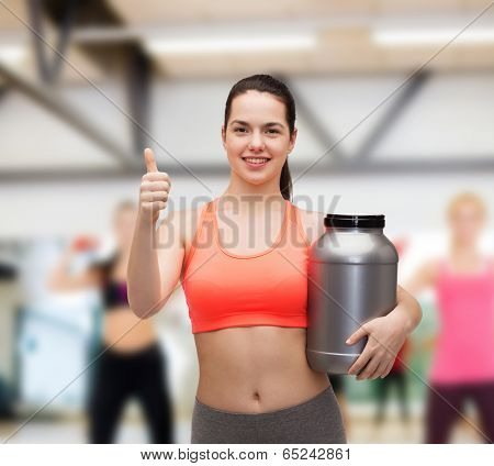 fitness and diet concept - smiling teenage girl with jar of protein showing thumbs up