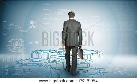 Businessman in suit holding briefcase and goes forward. Rear view. Wire-frame gears gear underfoot