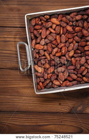 roasted cocoa chocolate beans in Vintage heavy cast aluminum roasting pan on wood background