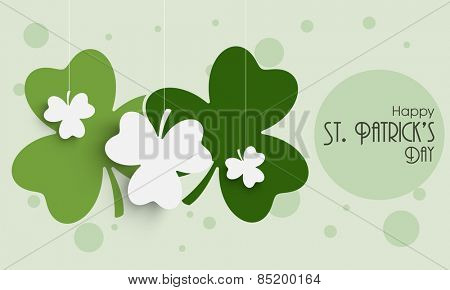 Happy St. Patrick's Day celebration with hanging clover leaves on green background.