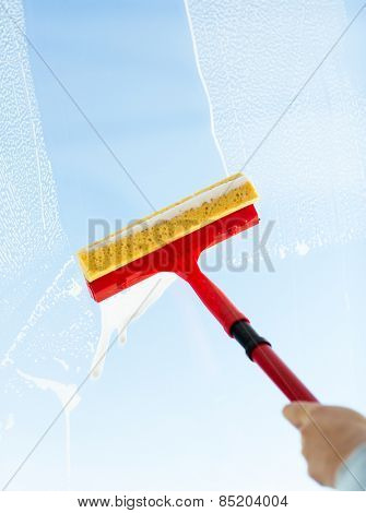 people, housework and housekeeping concept -close up of hand cleaning window glass with sponge mop and foam