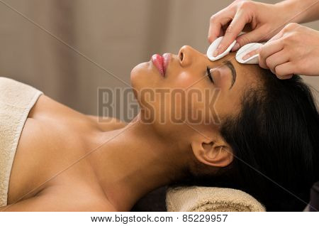 Young woman having face makeup removed with cotton swab 