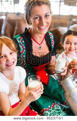Bavarian mother sitting with children in cowhouse on hay bale drinking fresh milk