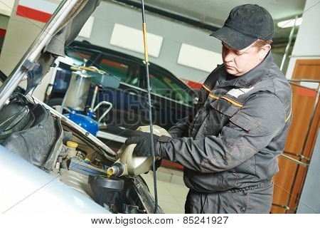 auto mechanic technician replacing and pouring motor oil into automobile engine at maintenance repair service station