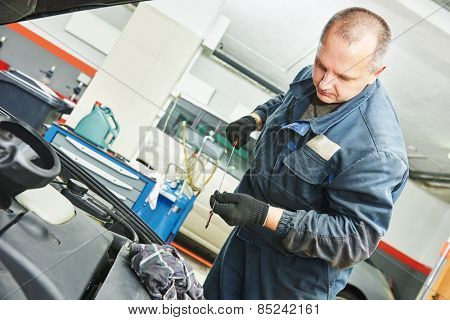 Auto mechanic checking oil level in car engine at garage service station