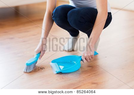 people, housework, cleaning and housekeeping concept - close up of woman with brush and dustpan sweeping floor at home