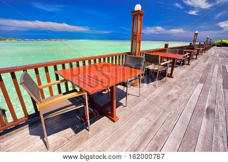 Chairs And Tables With Palm Trees, Water Bungalows And Clear Water On Luxorious Bech Resort.