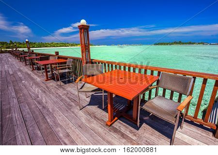 Chairs And Tables With Palm Trees, Water Bungalows And Clear Water On Luxorious Bech Resort.
