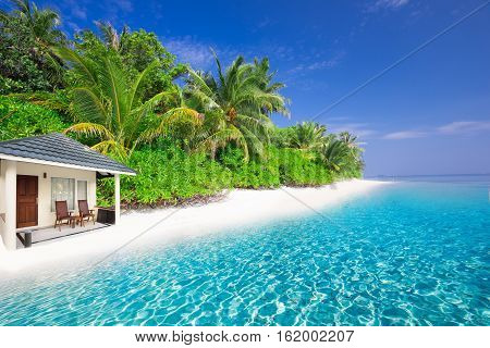 Overwater Bungalows On Tropical Island With Sandy Beach, Palm Trees And Turquoise Clear Water