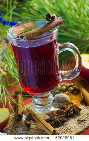 Spicy Christmas drink in a glass with spices on a background of trees