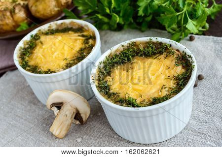 Hot dish of mushrooms chicken baked in a creamy sauce (bechamel) under a cheese crust green decoration in small ceramic bowls on a dark background. Russian "julienne".
