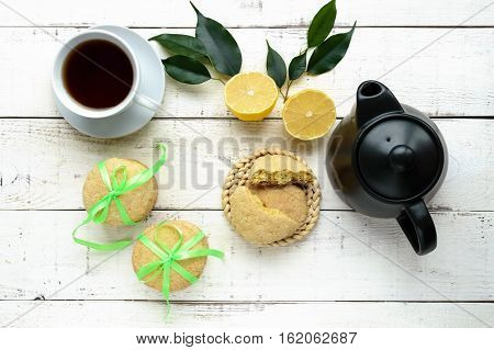 Shortbread lemon flavored cookies: a broken and connected green ribbon for a gift. Teapot and fresh lemon on a white wooden background. The top view.
