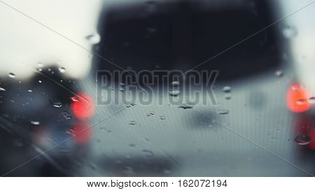 Car glass on a rainy day - defocused background. Moving waterdrops in the wipers of the windshield, close up, horizontal