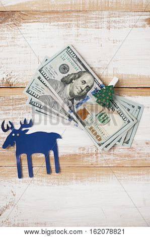 One hundred dollar bills with clothespins decorated Christmas trees and dark blue paper deer. Flat lay