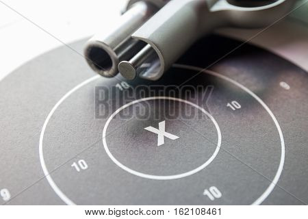close up ' x ' on bullseye paper shooting target with blurred silver .45 pistol barrel background