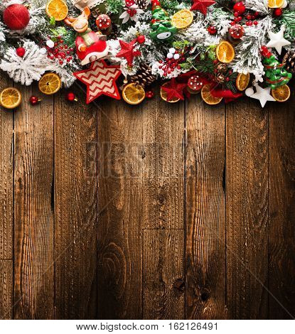 Merry Christmas Frame with green pine, colorful baubles, knots with berries,stars, orangesand other seasonal stuff over an old wooden aged background