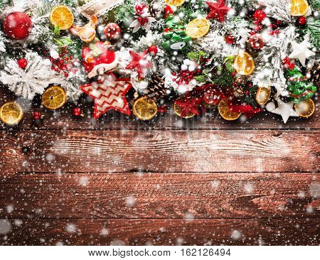 Merry Christmas Frame with Snow and wood green pine, colorful baubles, knots with berries,stars, orangesand other seasonal stuff over an old wooden aged background