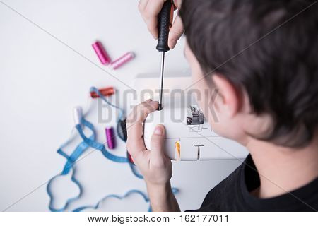 Man with screwdriver repairing sewin-machine