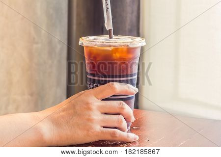 Woman's hand holding iced coffee in takeaway cup.