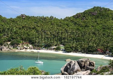 white sailboat anchred in beautiful crystal bay surrounded by jugle clad hills near lamai on ko samui island in the gulf of thailand