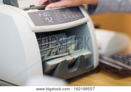 people, finance and cash concept - clerk hand counting dollars with electronic money counter machine at bank office or currency exchanger