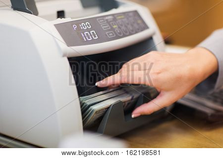 people, finance and cash concept - clerk hand counting dollars with electronic money counter machine at bank office or currency exchanger