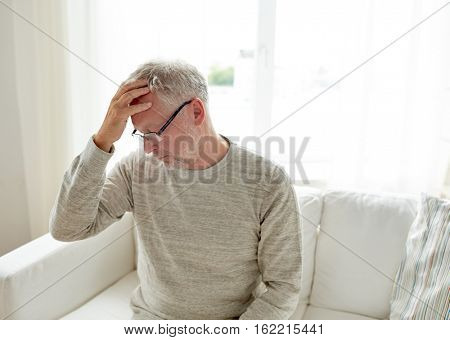 healthcare, pain, stress, age and people concept - senior man suffering from headache at home
