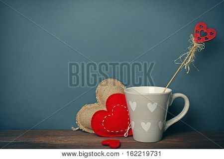 Cup with color hearts on wooden table against grey background